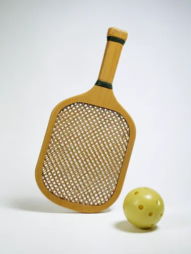 front-view of a wooden pickle ball racket and ball, racket is leaning on the side on white seamless background, no distractions, directional lighting with a clean shadow, high quality studio photogrpahy   --raw