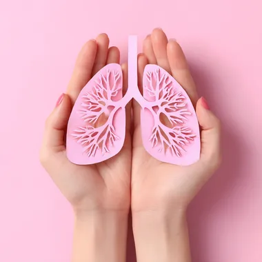 Female hands holding paper lungs on pink background. Lung cancer concept