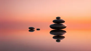 four stacked flat zen stones on a reflective surface at sunrise, soft orange-pink sky, reflective surface and sky should dominate, silent image, stones flat and small, peaceful minimalist composition, gentle gradient lighting, calm atmosphere, smooth textures  a2dpl3p   --s 22