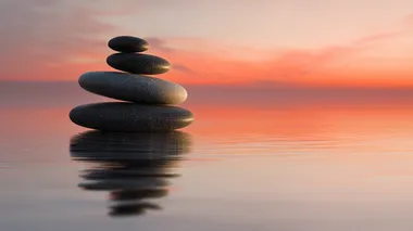 four stacked flat zen stones on a reflective surface at sunrise, soft orange-pink sky, reflective surface and sky should dominate, silent image, stones flat and small, peaceful minimalist composition, gentle gradient lighting, calm atmosphere, smooth textures  a2dpl3p   --s 22