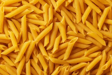 Top view of a large pile of uncooked yellow penne pasta, dry Italian pasta scattered randomly, seamless food texture, high detail, sharp focus, studio lighting, isolated background