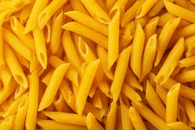 Top view of a large pile of uncooked yellow penne pasta, dry Italian pasta scattered randomly, seamless food texture, high detail, sharp focus, studio lighting, isolated background
