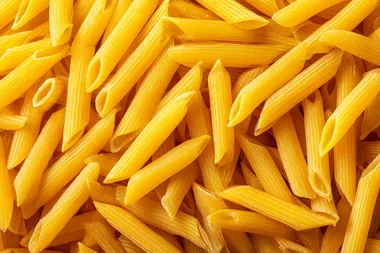 Top view of a large pile of uncooked yellow penne pasta, dry Italian pasta scattered randomly, seamless food texture, high detail, sharp focus, studio lighting, isolated background