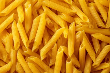 Top view of a large pile of uncooked yellow penne pasta, dry Italian pasta scattered randomly, seamless food texture, high detail, sharp focus, studio lighting, isolated background