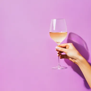 from the right comes a woman's hand holding a glass of wine, the background is pastel purple with a lot of lighting, real photo from stock rofile eps2b4q