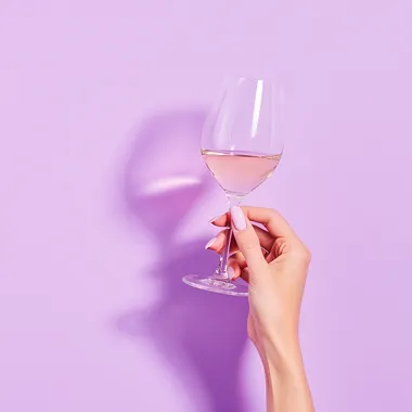 from the right comes a woman's hand holding a glass of wine, the background is pastel purple with a lot of lighting, real photo from stock rofile eps2b4q