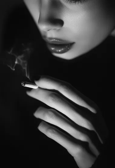 A close-up of the woman's hand, holding her cigarette between two fingers with light illuminating it from behind, creating an atmosphere of mystery and intrigue. The background is blurred to focus on the details of her hands, adding depth and texture to the overall composition. The black and white photography style adds contrast and intensity, highlighting the dramatic effect of the lighting. The woman is wearing .