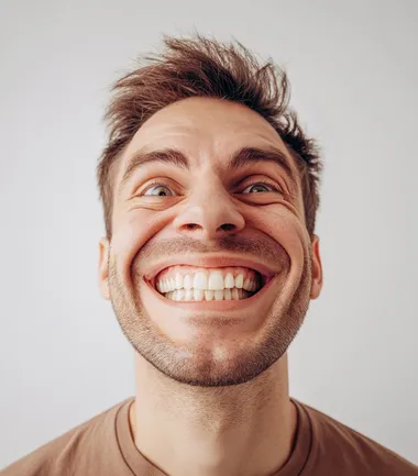 A photo of an attractive, smiling man with his face distorted into the shape of a large, exaggerated smile. The background is white, and he has short hair. He appears to be in good health based on the well-lit appearance. His facial features look normal, but the chin piece that forms part of the big smile makes him appear more handsome than cool or cute. It's like a humorous stock photo of someone having fun by changing their jawline for the portrait. Real person, solid stark white background, summer light.