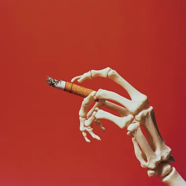 A cigarette with the end being pulled out by a skeleton hand, against a solid red background, in the style of product photography.
