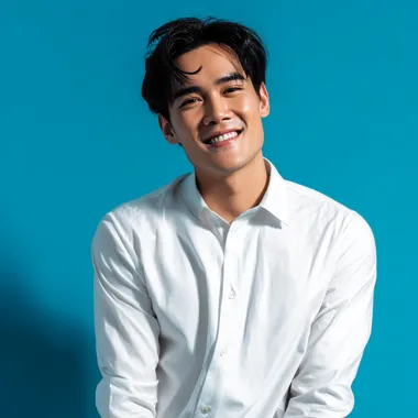 A 25-year-old Thai man, a handsome model, smiles confidently with his thick, dark hair. He is wearing a white dress shirt and posing naturally. The photo is a half-body shot with a vibrant blue background, taken in a studio. The high-resolution image captures every detail. wide lend, realistic details.