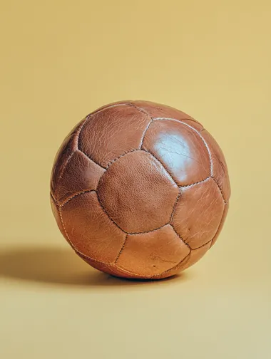 A classic vintage leather soccer football, minimal pastel yellow background, retro cinematic lighting, nostalgic poster style, centred composition, soft shadows, subtle grain, bold yet minimal   --raw rofile lia5zav k5ni7kr