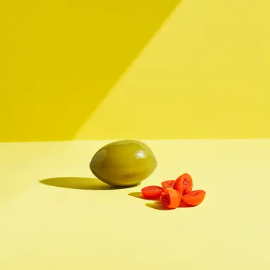 Straight on, very low eye level camera angle. Showcasing the side view of a half olive. add a group of three small chopped pieces red pimento next to the olive. Natural and soft lighting. Daylight bright setting. Placed on a yellow background. --s 50