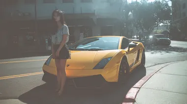 A casual smartphone snapshot of an East Asian woman in a short miniskirt stepping out of a yellow Lamborghini Huracn. Bright daylight, street parking, slightly tilted angle, realistic shadows, no filters.