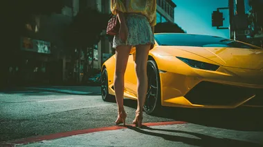 A casual smartphone snapshot of an East Asian woman in a short miniskirt stepping out of a yellow Lamborghini Huracn. Bright daylight, street parking, slightly tilted angle, realistic shadows, no filters.