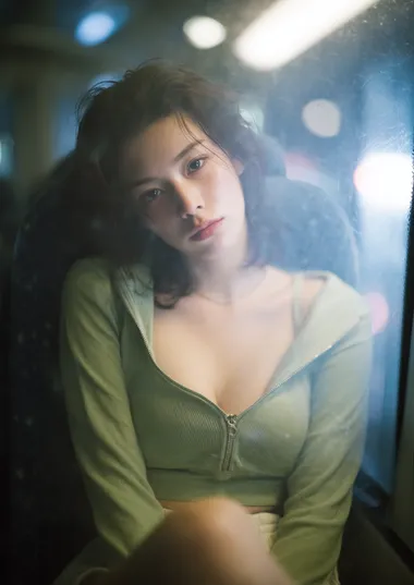 photo of a young Korean woman in an olive green zip-up fitted cropped top and shorts, slouched near the window of an intercity night bus, seen through the foggy glass from outside or between two high seatbacks, faint LED reading light above casting cold glow on her jawline and collarbone, reflections of distant taillights across the window, hair in soft motion as the bus bumps slightly, a pillow resting near her side, completely unaware, voyeurism style, Fujifilm X-T5 with 56mm f/1.2 lens  --raw --exp 15   8drdw5o