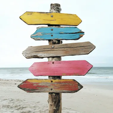 wooden signpost on the beach. There are colorful signs on the sign: pink, yellow, blue, turquoise. white background