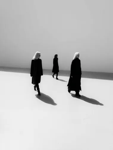 Three people walking on a white floor, shadows, wearing black clothes and contrasting with the background, no shadow, white clean background, Looking at different places, one person is in agony  rofile eo8b66r