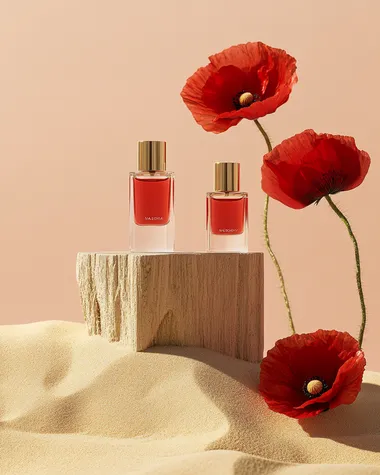A minimalist product shot for a perfume sample brand with a red and white color palette and gold accents. Four clear small sample bottles sit on an abstract, textured podium made of wood and sand. The scene includes two poppies in front of it, symbolizing beauty and nature. The background is a soft peach color. The overall vibe conveys a sense of elegance and high quality.