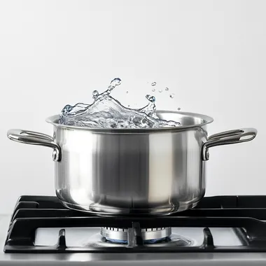 A realistic SIDE view photo of a stainless steel pot on a gas stove with boiling water inside, visible steam rising. White background, high-quality food photography