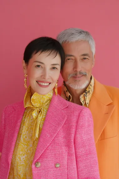 a front shot of a lovely, modern, cheerful. good looking 70 years old asian model couples in a young modern look, pink and orange blazer  o9smv9f