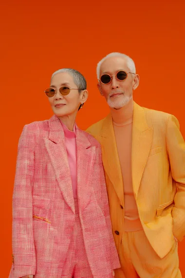 a front shot of a lovely, modern, cheerful. good looking 70 years old asian model couples in a young modern look, pink and orange blazer  o9smv9f