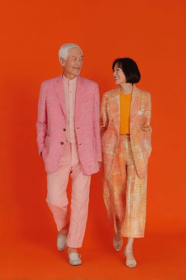 a front shot of a lovely, modern, cheerful. good looking 70 years old asian model couples in a young modern look, pink and orange blazer  o9smv9f