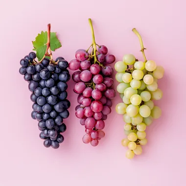 detailed photo of red wine grape, white wine grape and pink wine grape over a pink background
