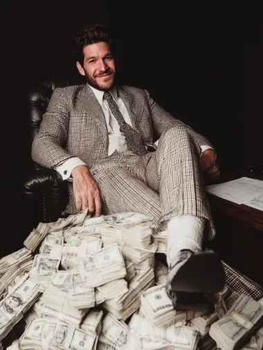 spotlight on a white businessman in suit sitting with shoes up on desk smiling, his desk is full on piles of cash, black background   rofile ncdd2gx   --raw