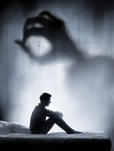 a person sitting on a bed with a giant shadowy hand pressing down on their shoulders, embodiment of anxiety, dark palette, high contrast, conceptual stock image  --raw rofile gq52qgq 6v2mwdg
