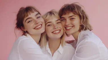 three beautiful women of European appearance hug and smile on a pink background. Several ladies in white shirts. Female friendship. High quality photo