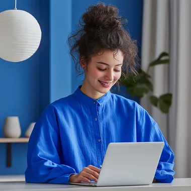 smiley person female working on the laptop in clean space with minimalistic interior, wearing blue shirt