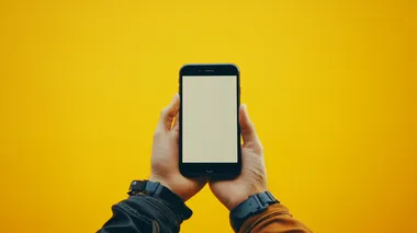 a frontal photo of a hand holding a blank iphone mockup. shot against a yellow studio backdrop. in the style of product photography. photorealism, hyper realistic, centered, symmetrical composition, extreme detail 8k style raw