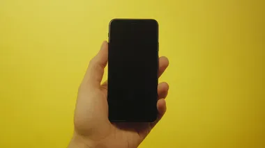 a frontal photo of a hand holding a blank iphone mockup. shot against a yellow studio backdrop. in the style of product photography. photorealism, hyper realistic, centered, symmetrical composition, extreme detail 8k style raw