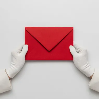 Two hands wearing white silk gloves holding an big red envelope, white background, top View