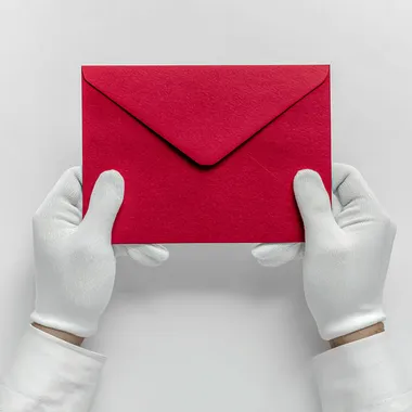 Two hands wearing white silk gloves holding an big red envelope, white background, top View