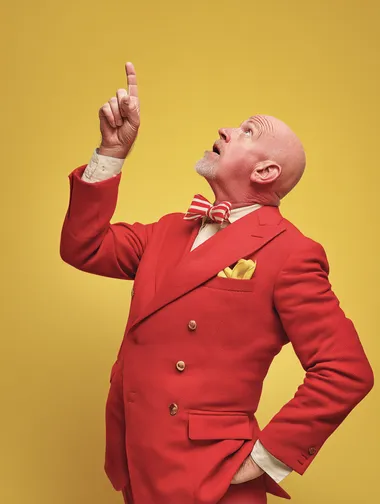 a middle aged man in a red suit pointing up, plain yellow background  rofile d8cpfrr