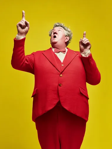 a middle aged man in a red suit pointing up, plain yellow background  rofile d8cpfrr