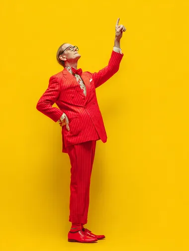 a middle aged man in a red suit pointing up, plain yellow background  rofile d8cpfrr