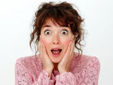 A woman with her hands on the cheeks, looking surprised and excited. She has brown hair and is wearing pink . white background   --s 250