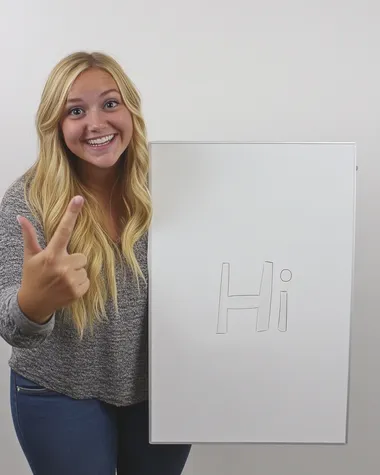 The 25-year-old blonde girl widened her eyes in surprise and looked down happily at the large whiteboard in her hand. the whiteboard was on the floor. One of her arms pointed to the whiteboard which is written 'Hi'. Her other hand was supported on the top of a large whiteboard. white backdrop, style raw