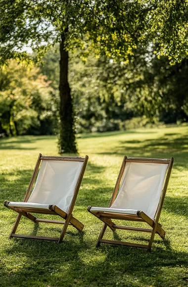 Two wooden garden chairs with white fabric on the lawn in front of trees, shot from a distance, on a sunny day, using a Nikon Z7 II and natural light.