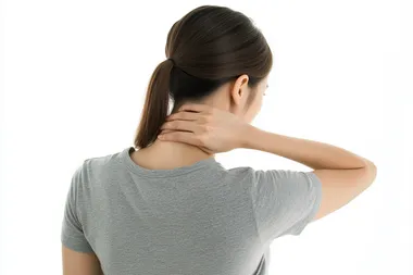 Photo of a Korean woman standing with her back to the camera, wearing a casual grey t-shirt. Her left hand gently touching the back of her neck, expressing mild discomfort, with natural posture and realistic hand positioning. Soft lighting, white background, no dramatic expression, photorealistic