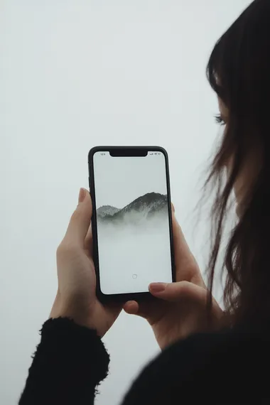 A woman holding an iPhone with a white screen, in the mockup style. The background is pure white and the focus of attention is on her hand holding up the phone. She has dark hair and appears to be in a profile view. Her fingers appear poised over the button that blends into the black frame of the phone, which she holds against a clean white backdrop. There is no visible text or other elements inside the smartphone display, highlighting its blank space for custom content or advertising copy. It is an ultra-realistic photograph captured at high resolution 32k.