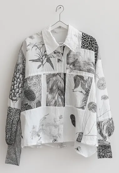 A white women's shirt hanging on the wall, with small areas of leopard print and fruit patterns printed on it, with irregular composition.  4249887665   --s 250