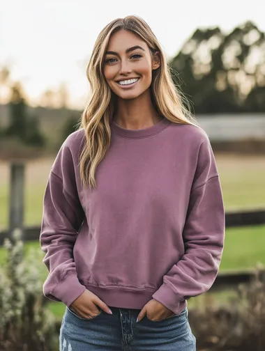 woman wearing an acid washed mauve colored crewneck sweatshirt. woman is smiling. woman is facing the camera. apparel mockup style. focus on the quality of the crewneck. background is a country scene.