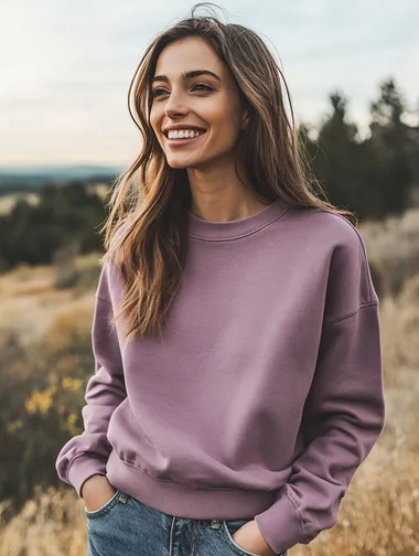 woman wearing an acid washed mauve colored crewneck sweatshirt. woman is smiling. woman is facing the camera. apparel mockup style. focus on the quality of the crewneck. background is a country scene.