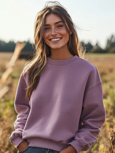 woman wearing an acid washed mauve colored crewneck sweatshirt. woman is smiling. woman is facing the camera. apparel mockup style. focus on the quality of the crewneck. background is a country scene.