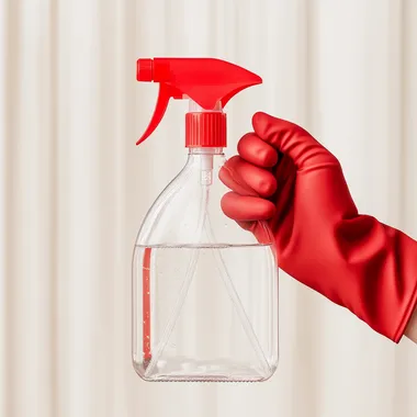 highly detailed product photo of a hand with a red latex glove on holding a clear spray bottle with a red nozzle. The bottle is half filled with clear still water. the background is a clean cream white gradient with bright natural light. photorealistic, 4K.