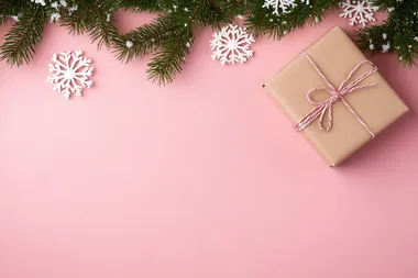 Christmas-themed pink background with white snowflakes, Christmas tree branches, and a gift box on a pastel pink tabletop. Flat lay style. Bright colors, high resolution. The concept of holiday celebration and shopping in the festive season. Stock photo with 2/3 space for text.  --s 50  sqq5bir