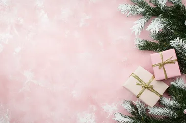 Christmas-themed pink background with white snowflakes, Christmas tree branches, and a gift box on a pastel pink tabletop. Flat lay style. Bright colors, high resolution. The concept of holiday celebration and shopping in the festive season. Stock photo with 2/3 space for text.  --s 50  sqq5bir